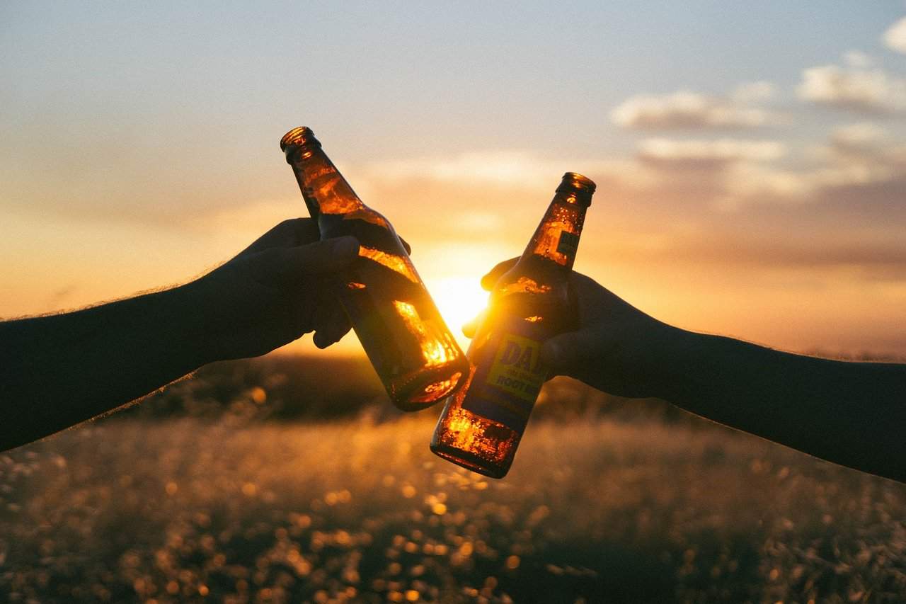 זוג ידיים משיקות בירה לרקע שקיעה